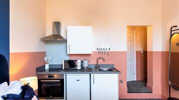 A compact kitchenette with a microwave, toaster, and small oven, a sink, and a cabinet above.