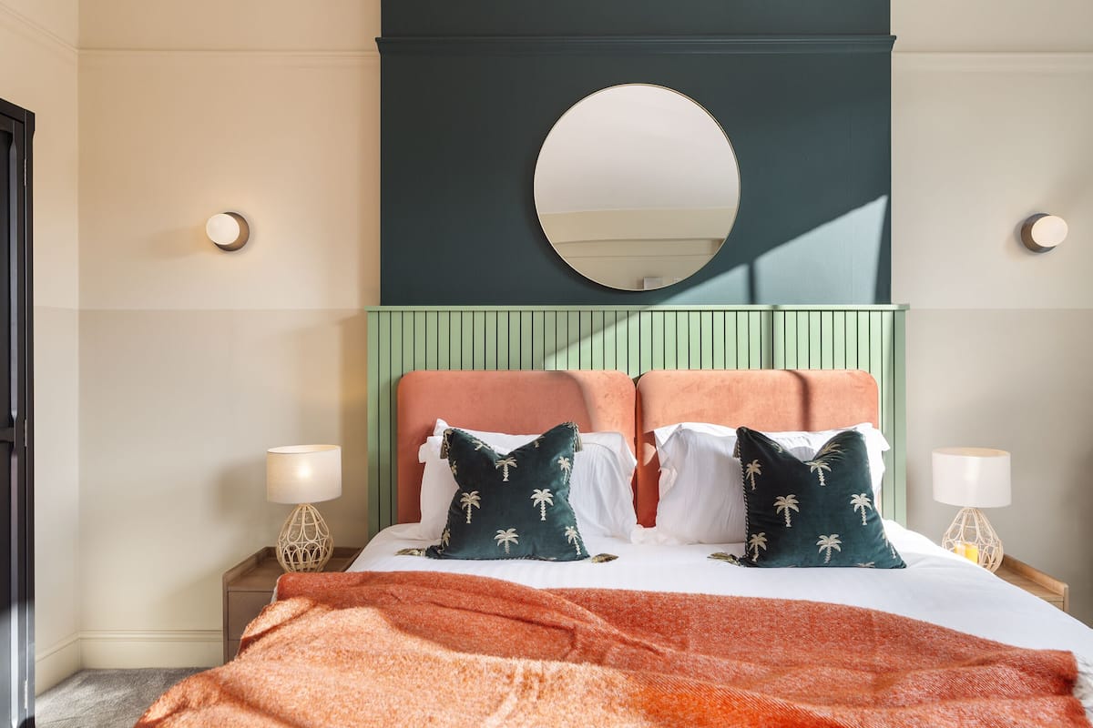 A neatly made bed with a green headboard, two white pillows, and a red blanket.