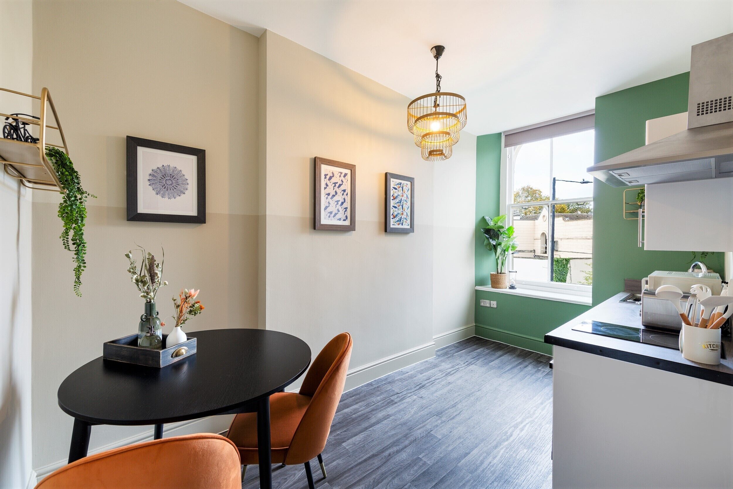 A modern kitchen with a dining area, featuring a black dining table, orange chairs, and a hanging light fixture.