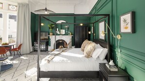 Un lit à baldaquin avec une couette blanche et beige, une petite table de chevet avec une lampe et un tableau encadré au mur.
