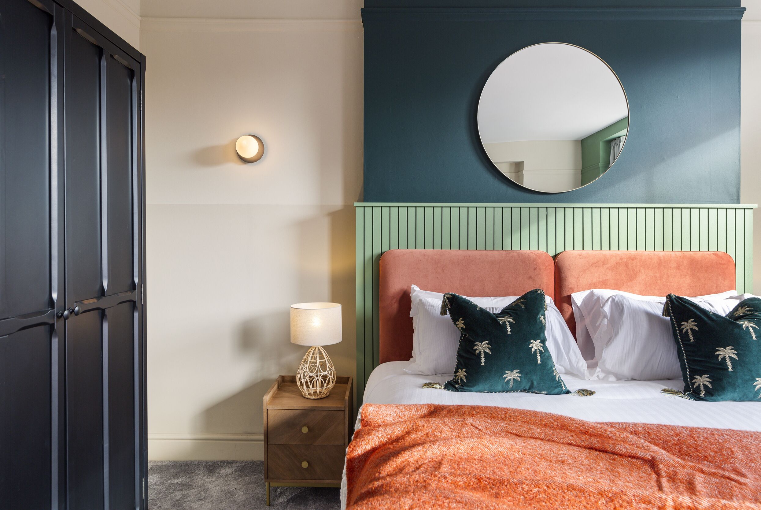 A bedroom with a bed, a nightstand, a lamp, a mirror, and a wardrobe.