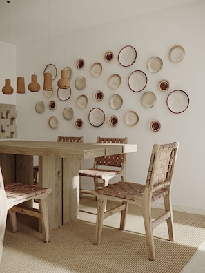 A dining area with a wooden table and chairs, a woven rug, and a wall decorated with various ceramic plates and pottery.