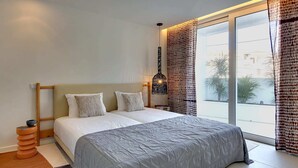 Ein modernes Schlafzimmer mit einem großen Bett, einem Nachttisch, einer Lampe und Blick ins Freie.