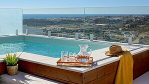 Ein Infinity-Pool auf dem Dach mit freiem Blick auf die Küstenlinie, einer Holzterrasse und einer Schale mit Gläsern und einer Karaffe.