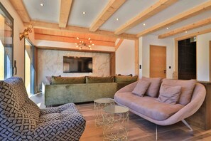A modern living room with a sectional sofa, a patterned armchair, and a glass coffee table. - Chalet Haut de Gamme 4* for 12pers with Jaccuzzi, Sauna+Gym (Les Orres)