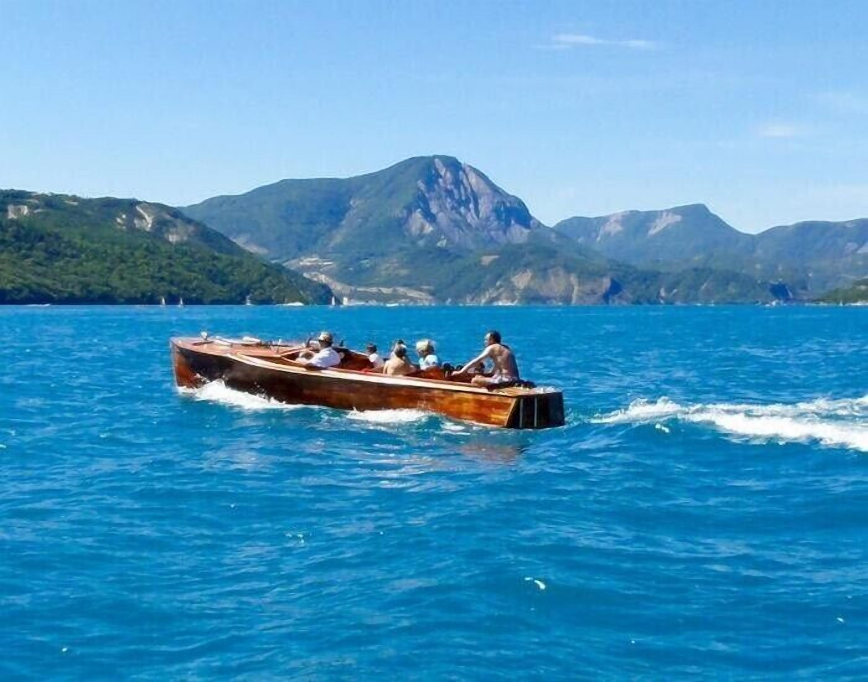A wooden boat with passengers on a calm lake, surrounded by mountains.