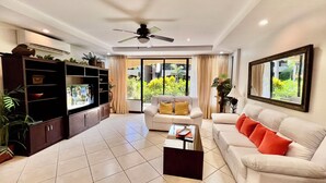 A living room with a TV, sofa, coffee table, and a ceiling fan. - Stay in the best located Vacation Condo in Jaco! (Jacó)