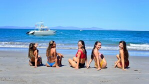 A group of five women sitting on a beach with a boat in the background. - Stay in the best located Vacation Condo in Jaco! (Jacó)