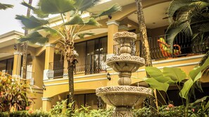 A multi-story building with balconies, a central fountain, and lush tropical plants.