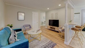 A living room with a blue sofa, a coffee table, a TV, and a dining area with wicker chairs. - ★ Good Vibes Ranch ★ Walk to Zoo | Pet Friendly (West Columbia)