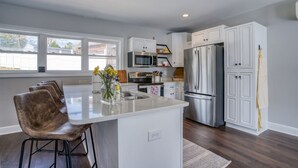 Una cocina moderna con armarios blancos, electrodomésticos de acero inoxidable y una isla central con taburetes de bar.