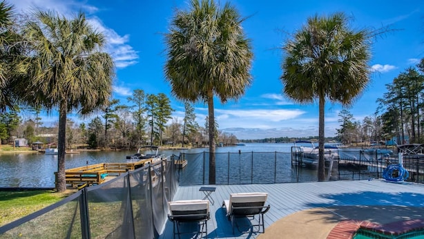 Terraza con dos sillas, piscina y vista a un lago con palmeras.