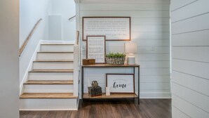 Una escalera que lleva a un rellano con una cita enmarcada y una pequeña mesa con objetos decorativos.