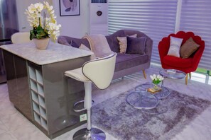 A modern living room with a grey sofa, a red armchair, a white bar stool, and a small round table with a vase of flowers. - Luxury Apartment With sea View in Lekki/ajah (Lekki)
