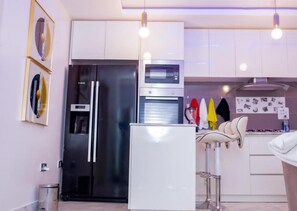 A modern kitchen with stainless steel appliances, a white refrigerator, and a bar area with stools. - Luxury Apartment With sea View in Lekki/ajah (Lekki)