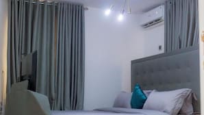 A bedroom with a bed, curtains, a ceiling light fixture, an air conditioning unit, and a television, a television, and a small table. - Luxury Apartment With sea View in Lekki/ajah (Lekki)