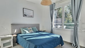A bedroom with a bed, bedside tables, a nightstand, a lamp, a window with curtains, and a framed picture on the wall.