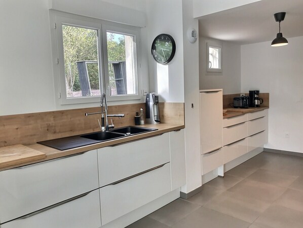 A modern kitchen with a wooden countertop, white cabinetry, a black clock, and a hanging pendant light. - Villa between sea and golf with swimming pool for 9 people (Saint-Raphaël)