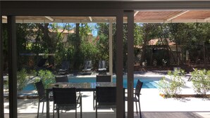A glass-enclosed patio with a pool, outdoor seating, and a view of a garden.