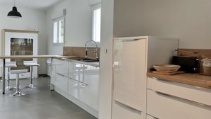 A modern kitchen with white cabinets, a stainless steel sink, and a black refrigerator. There are bar stools and a hanging light fixture.