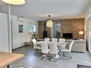 A modern living room with a dining area, a fireplace, and a staircase leading to an upper level.