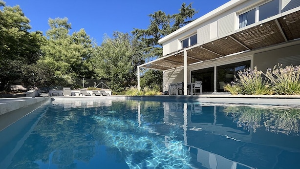 A modern house with a swimming pool, outdoor seating, and a covered patio area.