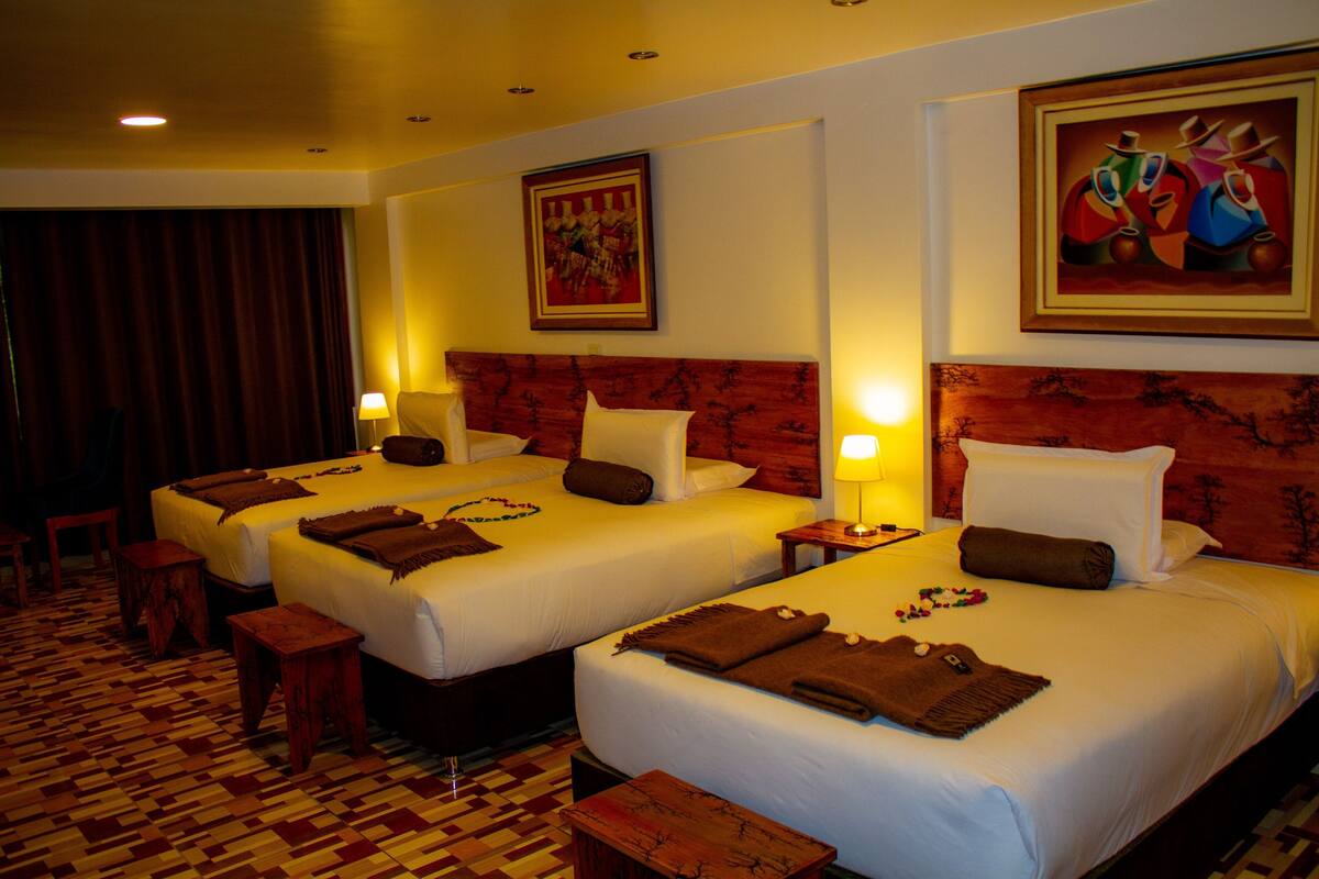 A hotel room with three beds, wooden headboards, and a patterned floor.