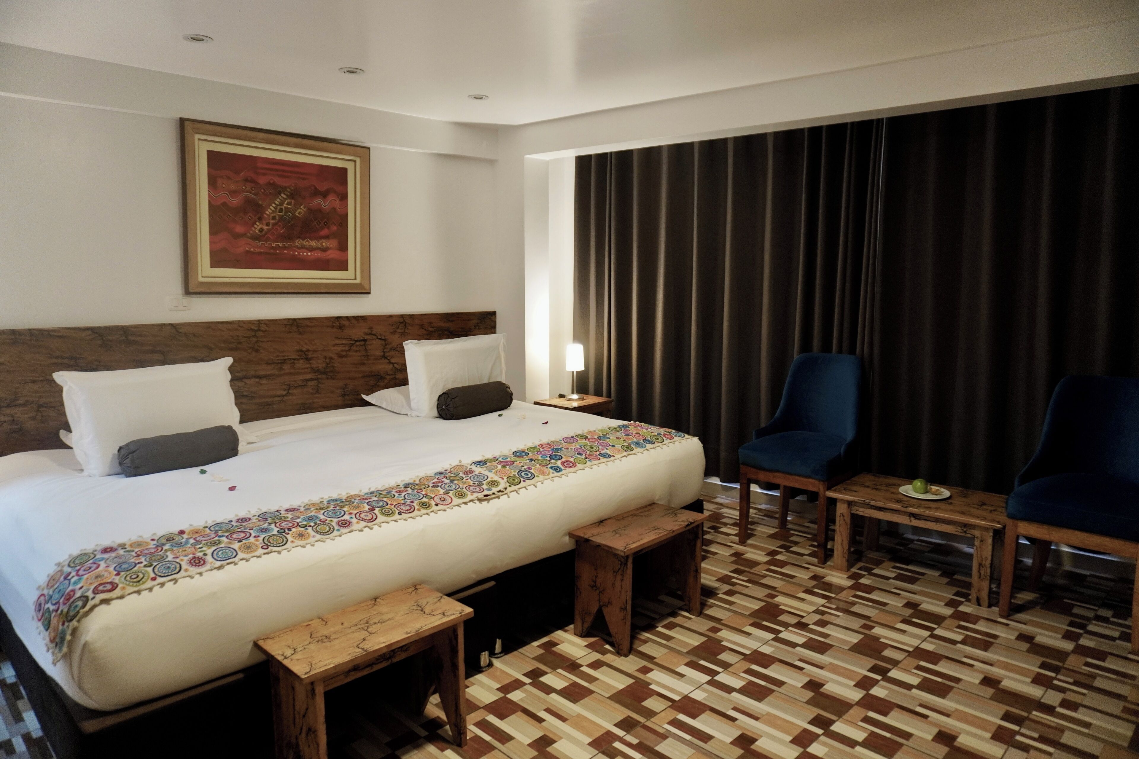 Una habitación de hotel con una cama grande, dos sillas, una mesita pequeña y un suelo con estampado.