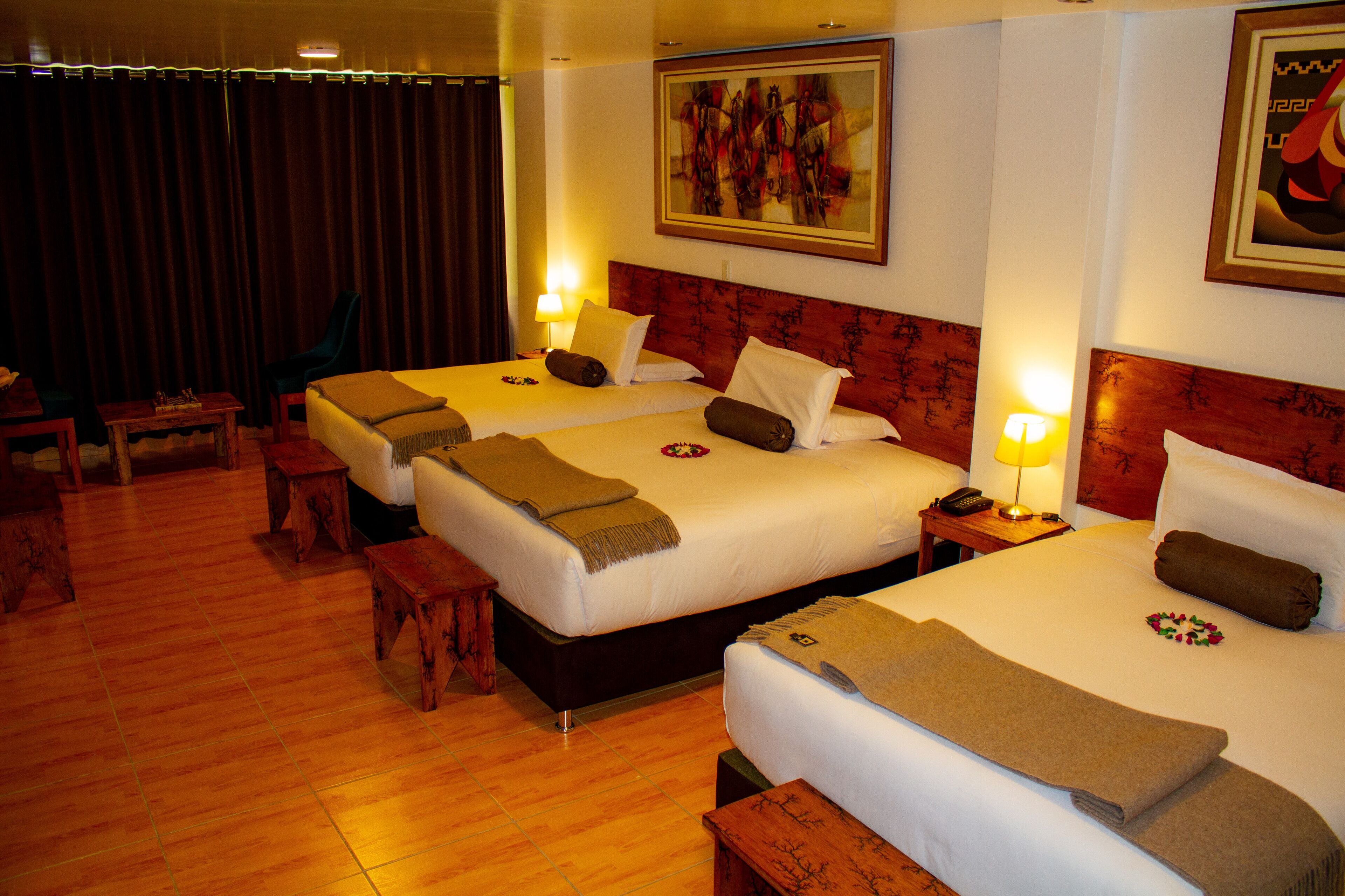 A hotel room with three beds, wooden furniture, and artwork on the walls.
