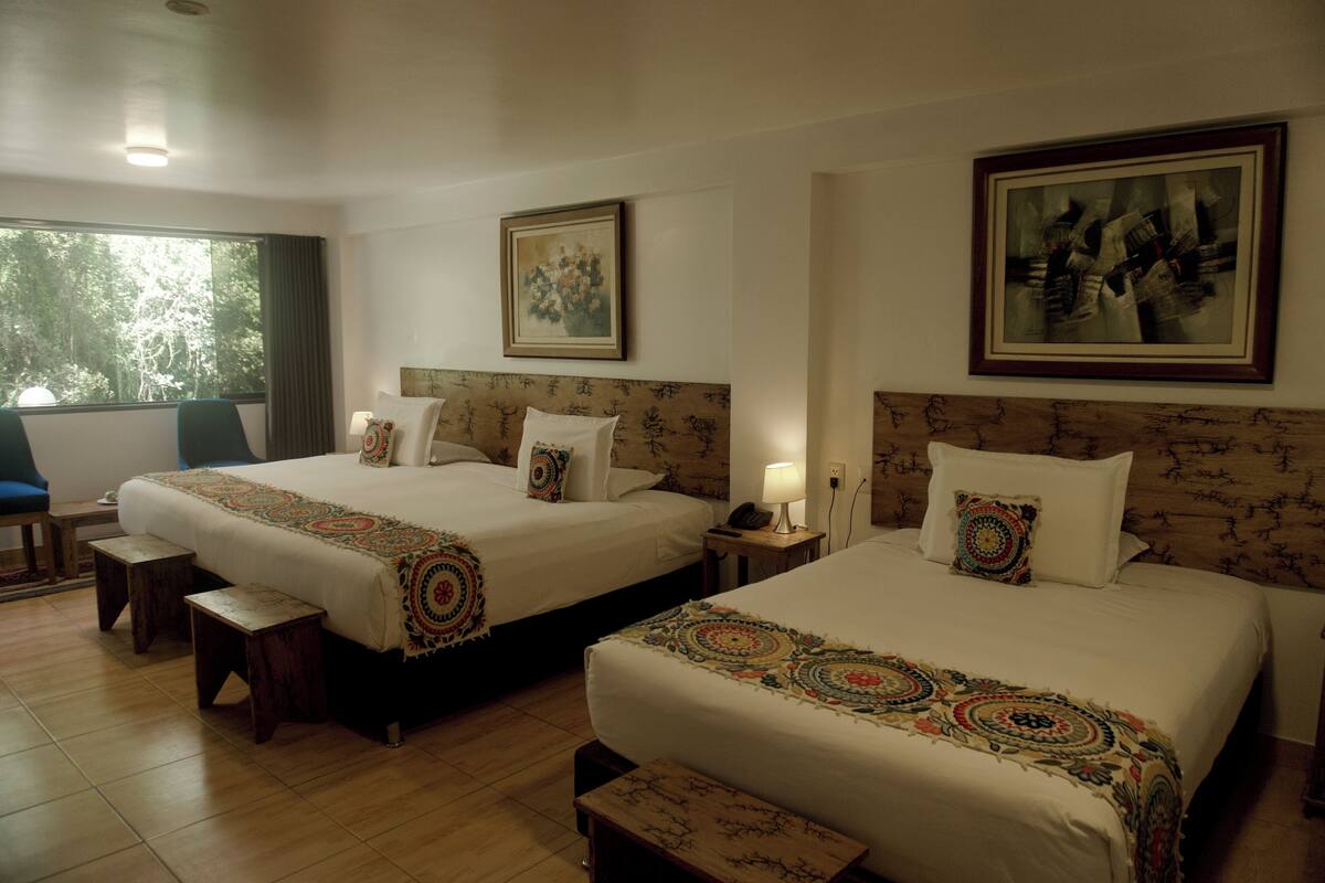 A hotel room with two beds, a large window, and a view of trees.
