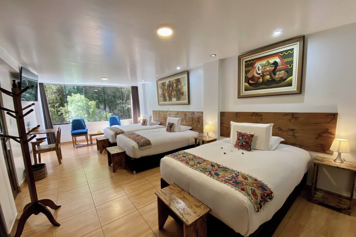 A hotel room with two beds, a dining area, and a view of greenery.