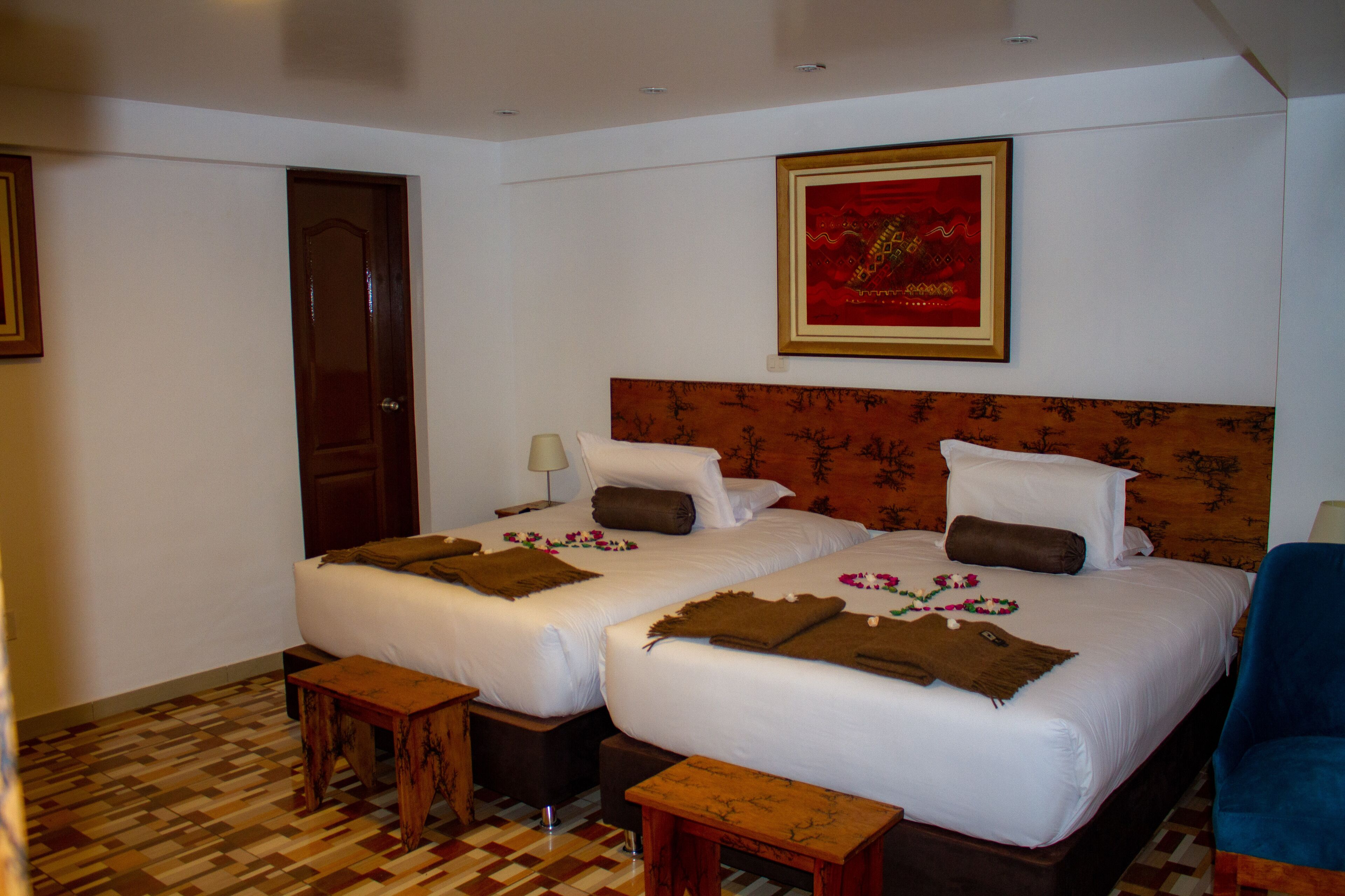 A hotel room with two beds, a wooden headboard, a framed picture on the wall, and a checkered floor.
