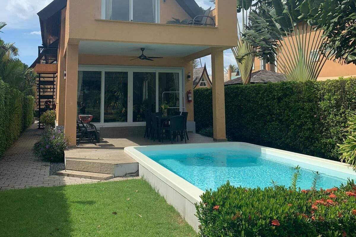 A two-story house with a swimming pool, a covered patio, and a garden.