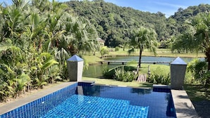 A swimming pool with blue mosaic tiles, surrounded by lush greenery and a view of a lake and hills. - Siam Royal View Pool Villa by PSR ASIA (Ko Chang)