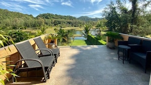 A terrace with lounge chairs and a view of a lake surrounded by greenery. - Siam Royal View Pool Villa by PSR ASIA (Ko Chang)