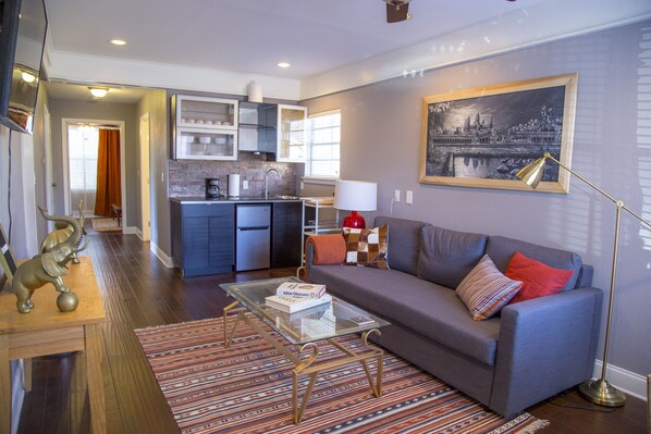 Relax in this stylish living space with a comfortable sofa, glass coffee table, and a large painting.