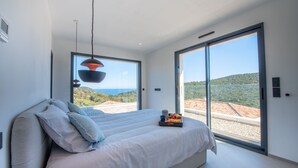 A modern bedroom with a large bed, a view of the landscape, and a tray with breakfast items. - Contemporary villa with pool and sea view for 10 people (Cavalaire-sur-Mer)