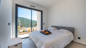 A modern bedroom with a large bed, a sliding glass door leading to a balcony, and a tray of fruit on the bed. - Contemporary villa with pool and sea view for 10 people (Cavalaire-sur-Mer)