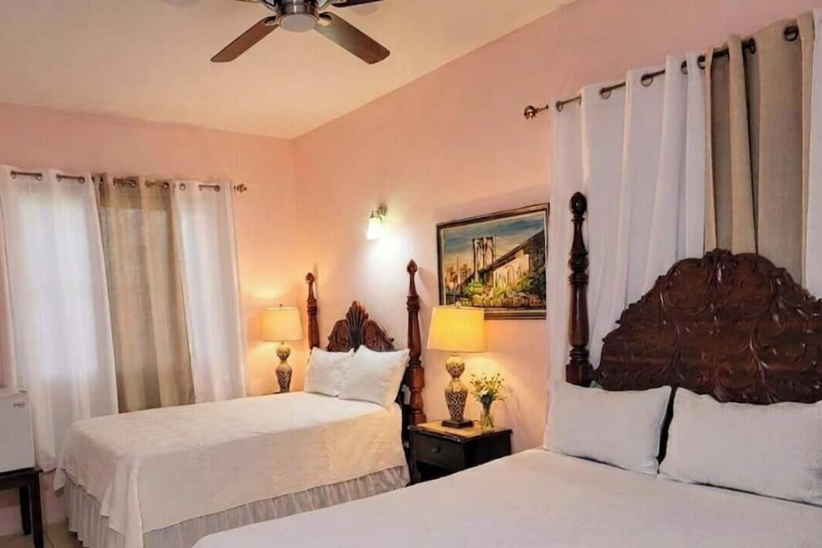 A hotel room with two beds, a ceiling fan, a painting, and a TV.