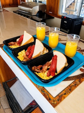 Un plateau de petit-déjeuner avec des œufs brouillés, du bacon, des toasts et du jus d’orange, posé sur un comptoir de cuisine.