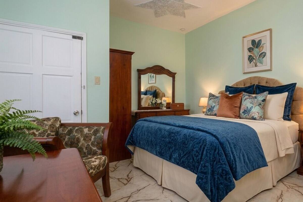 Une chambre à coucher avec un lit, une table de chevet, une lampe, une chaise et une plante.