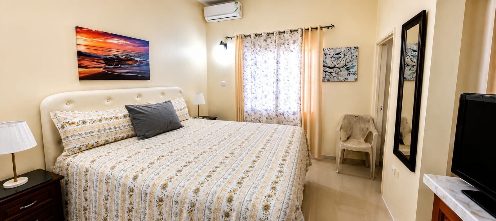 A bedroom with a bed, a chair, a TV, and artwork on the walls.