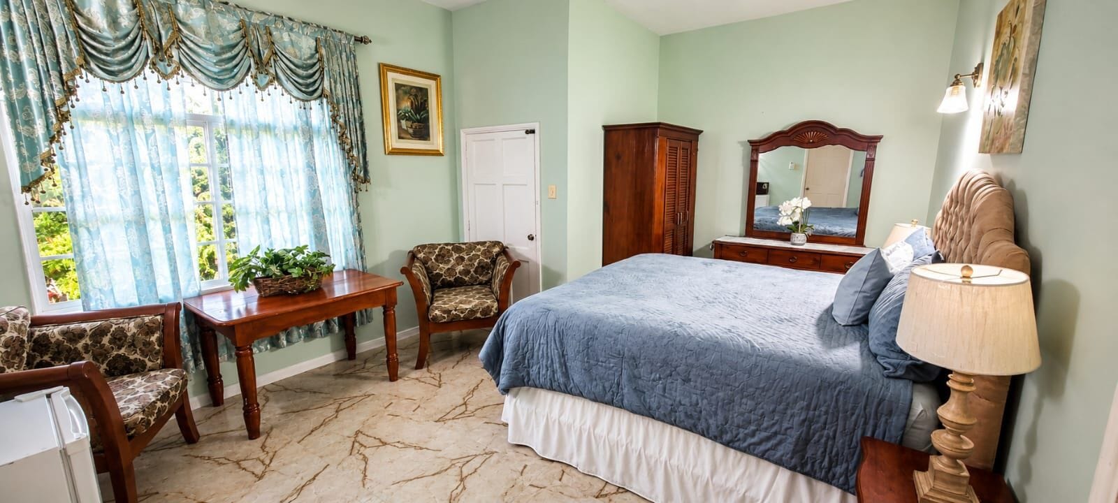 A bedroom with a bed, a chair, a table, a dresser, and a mirror.