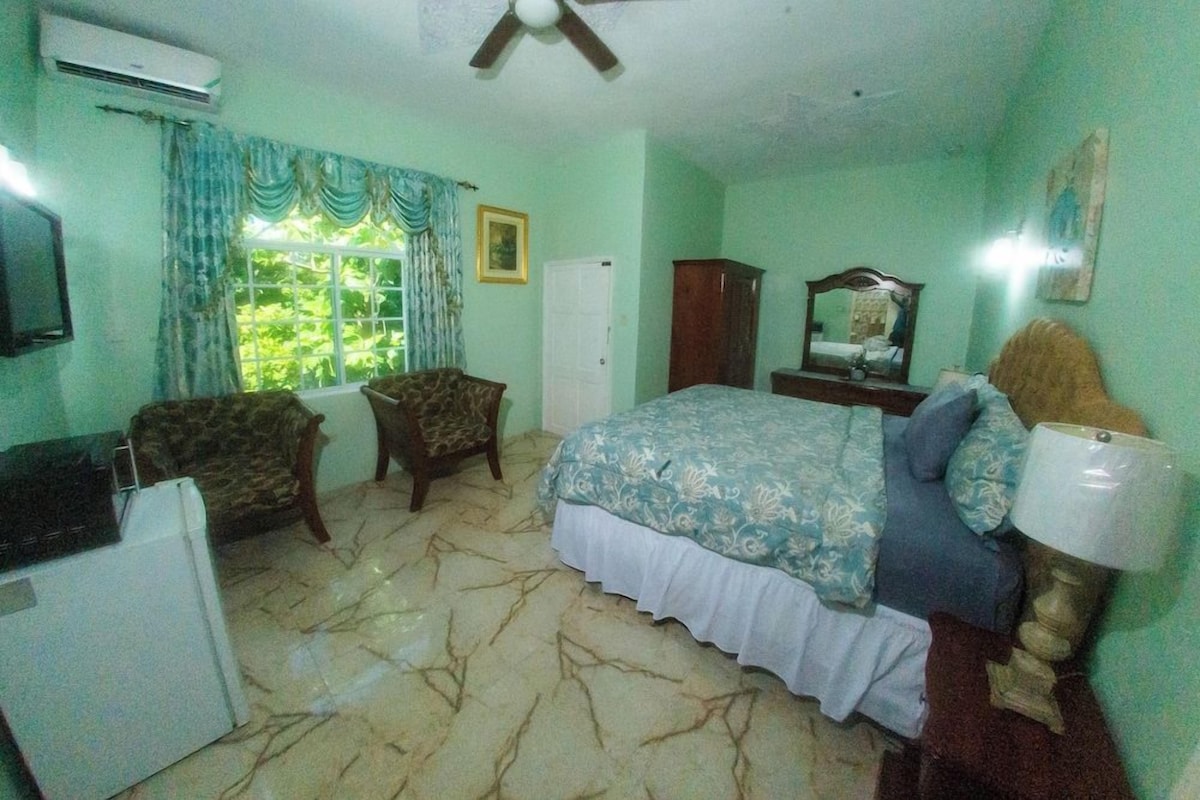 A bedroom with a bed, a chair, a desk, a mirror, and a window with curtains.