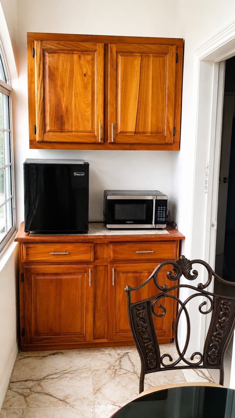 A compact kitchen with wooden cabinets, a black refrigerator, a microwave, and a metal chair.