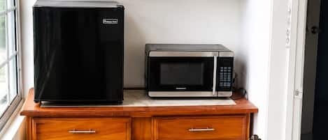 A compact kitchen with wooden cabinets, a black refrigerator, a microwave, and a metal chair.