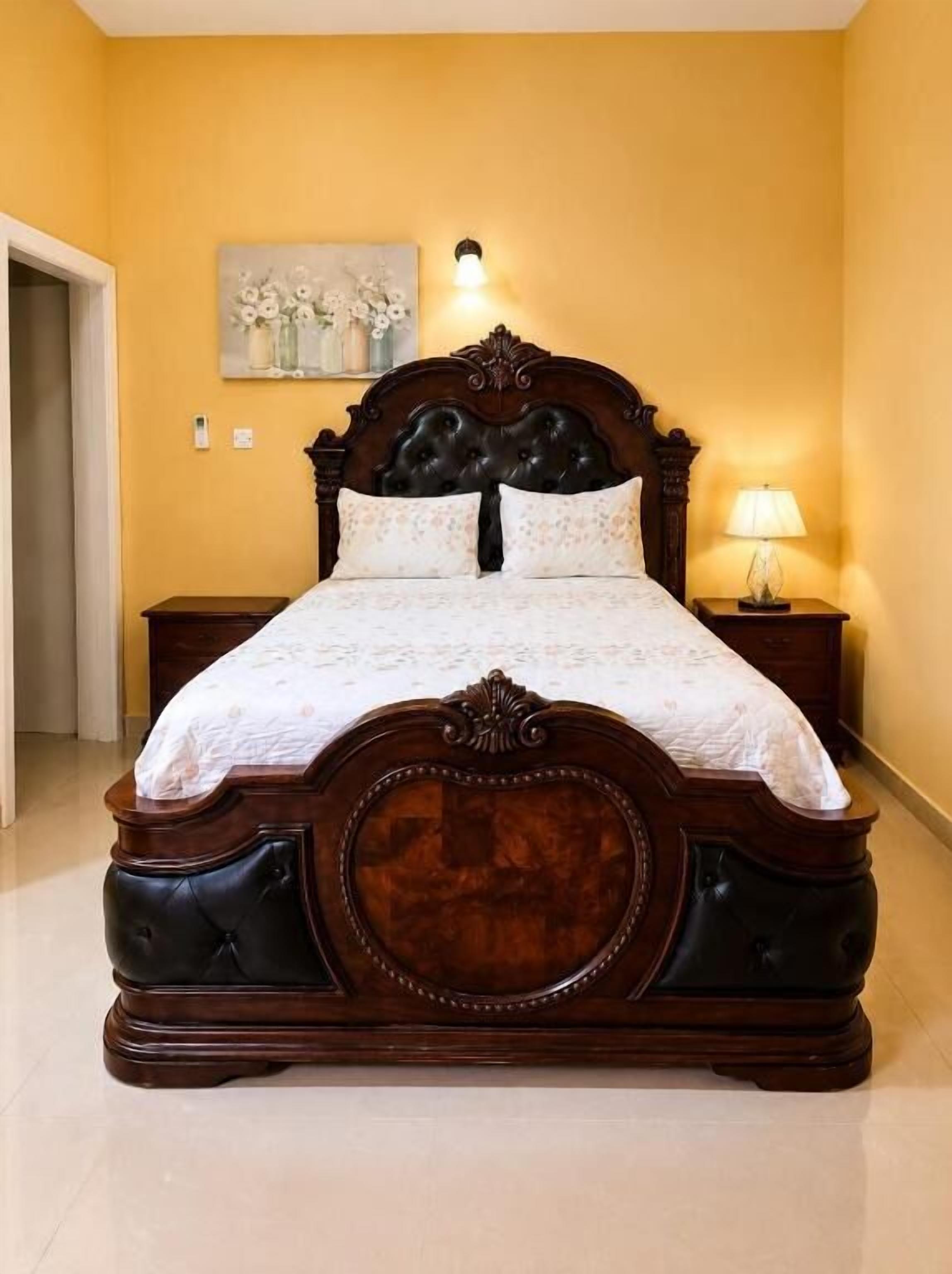 Un letto grande con testiera in legno, un comodino, una lampada a parete e un quadro appeso al muro.