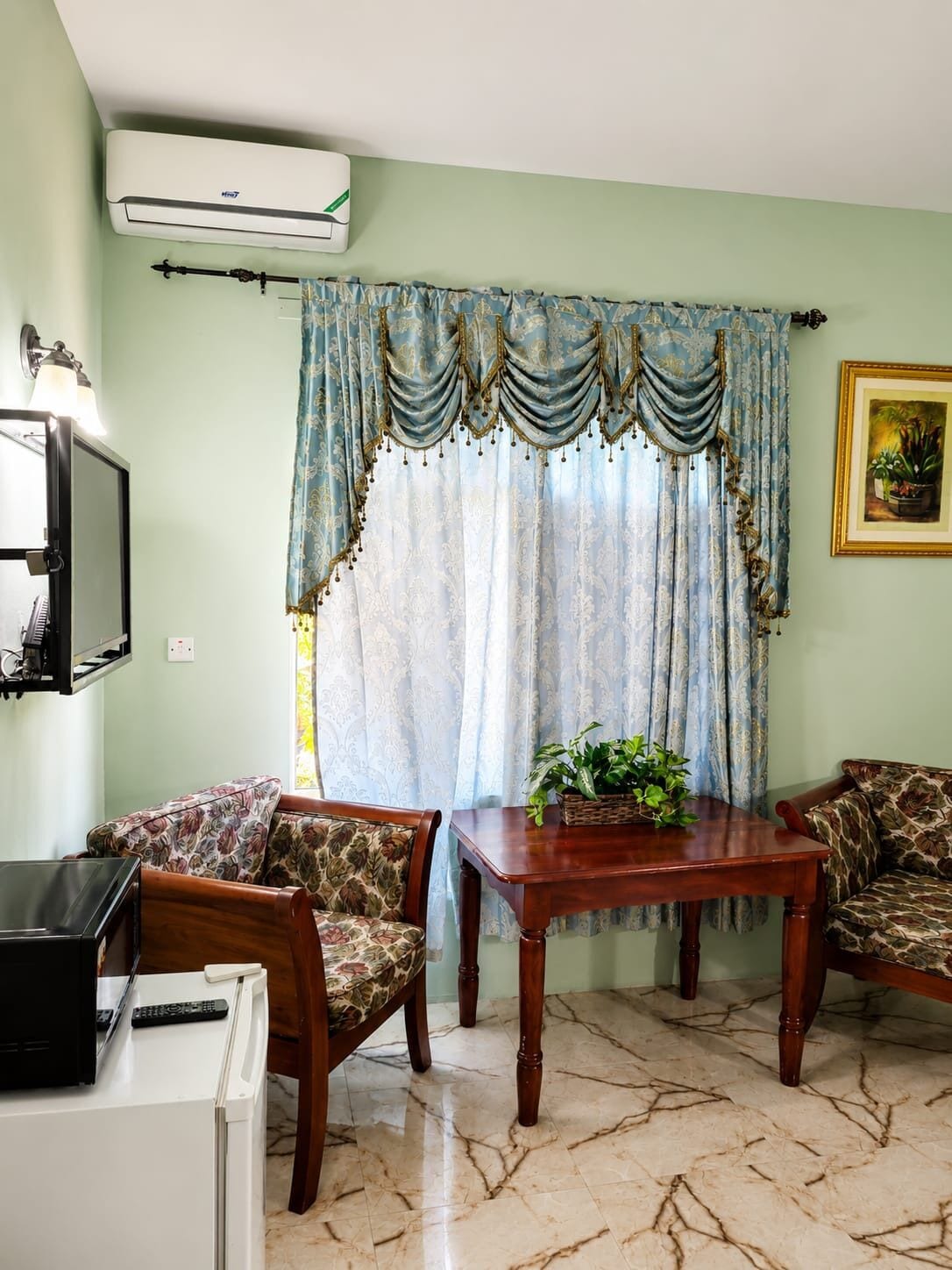 A living room with a TV, a table, two patterned sofas, a potted plant, and a window with curtains.