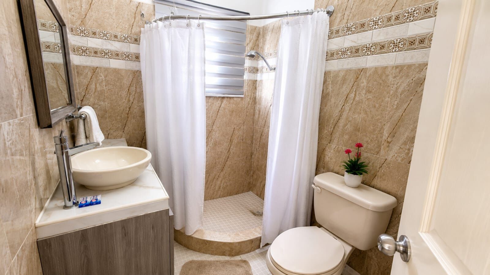 A bathroom with a sink, toilet, shower curtain, and a small potted plant.