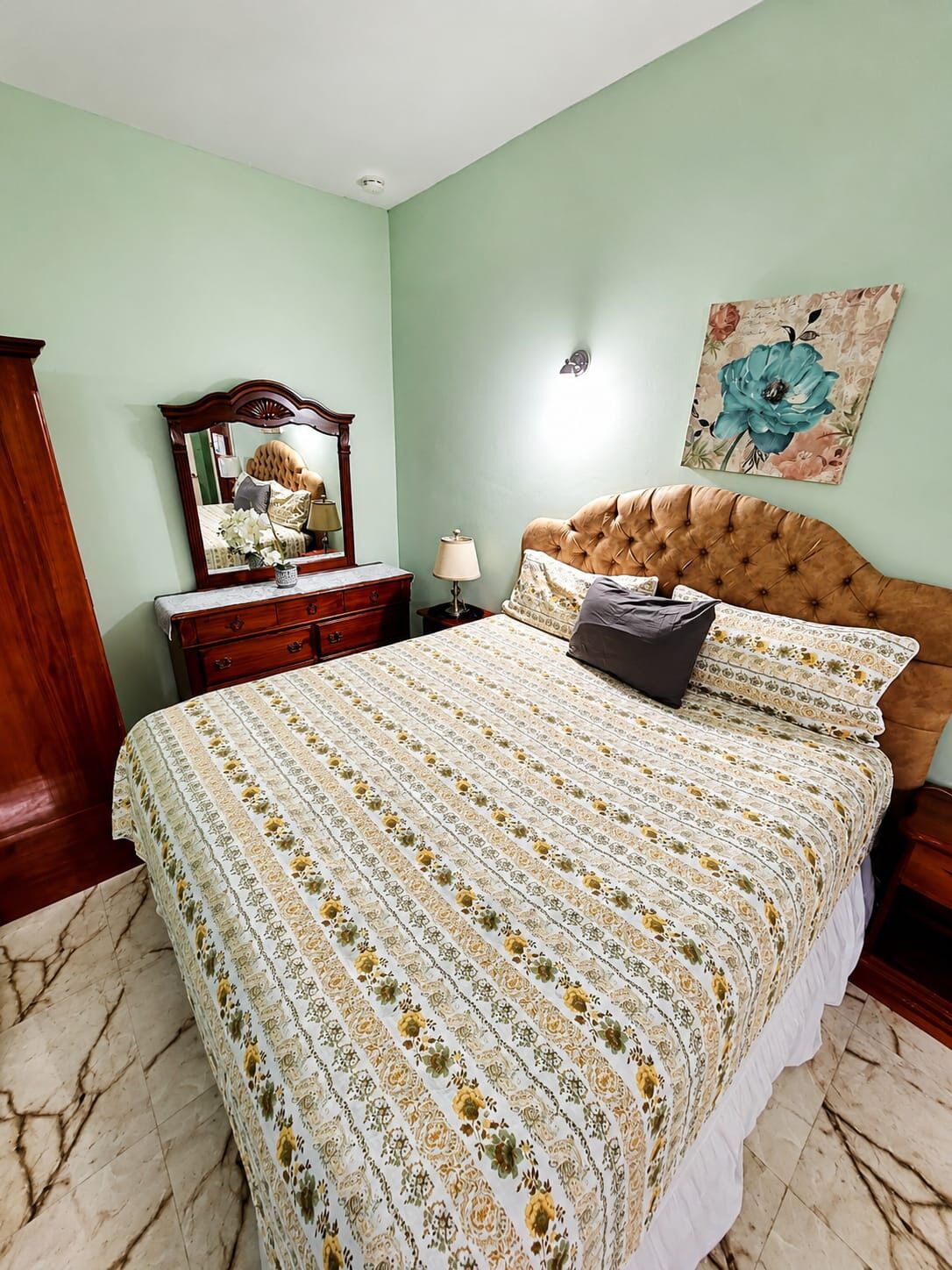 A bedroom with a bed, dresser, mirror, and a floral painting on the wall.